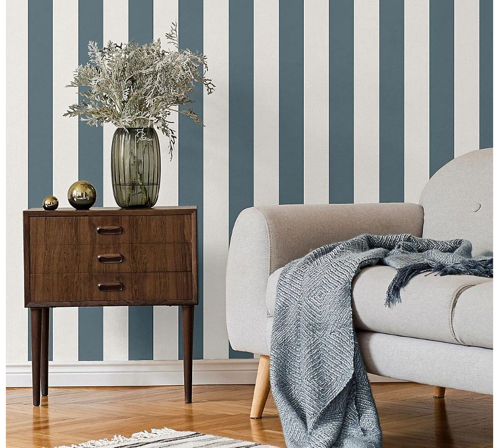 Giấy dán tường in hình lá màu vàng và xám trong phòng khách với ghế sofa màu be được trang trí bằng đệm và chăn màu vàng đậm.