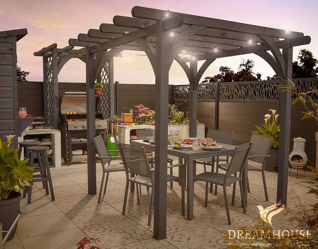 Giàn che màu xám che phủ bộ bàn ăn ngoài vườn, phía sau là bếp ngoài trời.