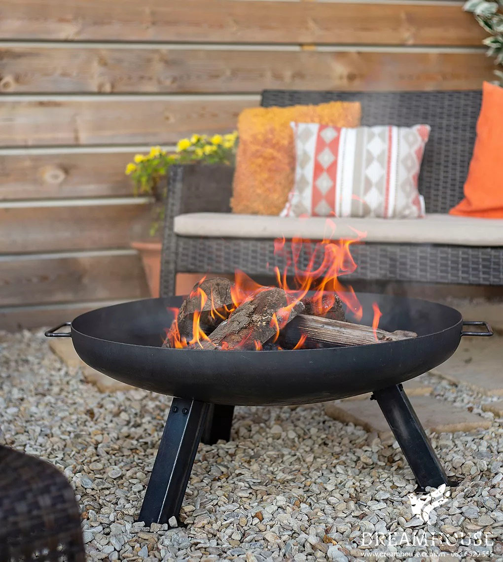 Hố lửa đen chứa đầy củi đang cháy, tỏa ra ánh sáng ấm áp khắp khu vườn.
